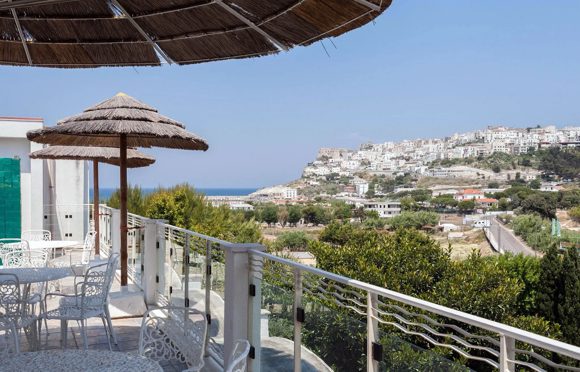 Terrazza con ombrelloni in paglia e vista panoramica sul borgo bianco e sul mare