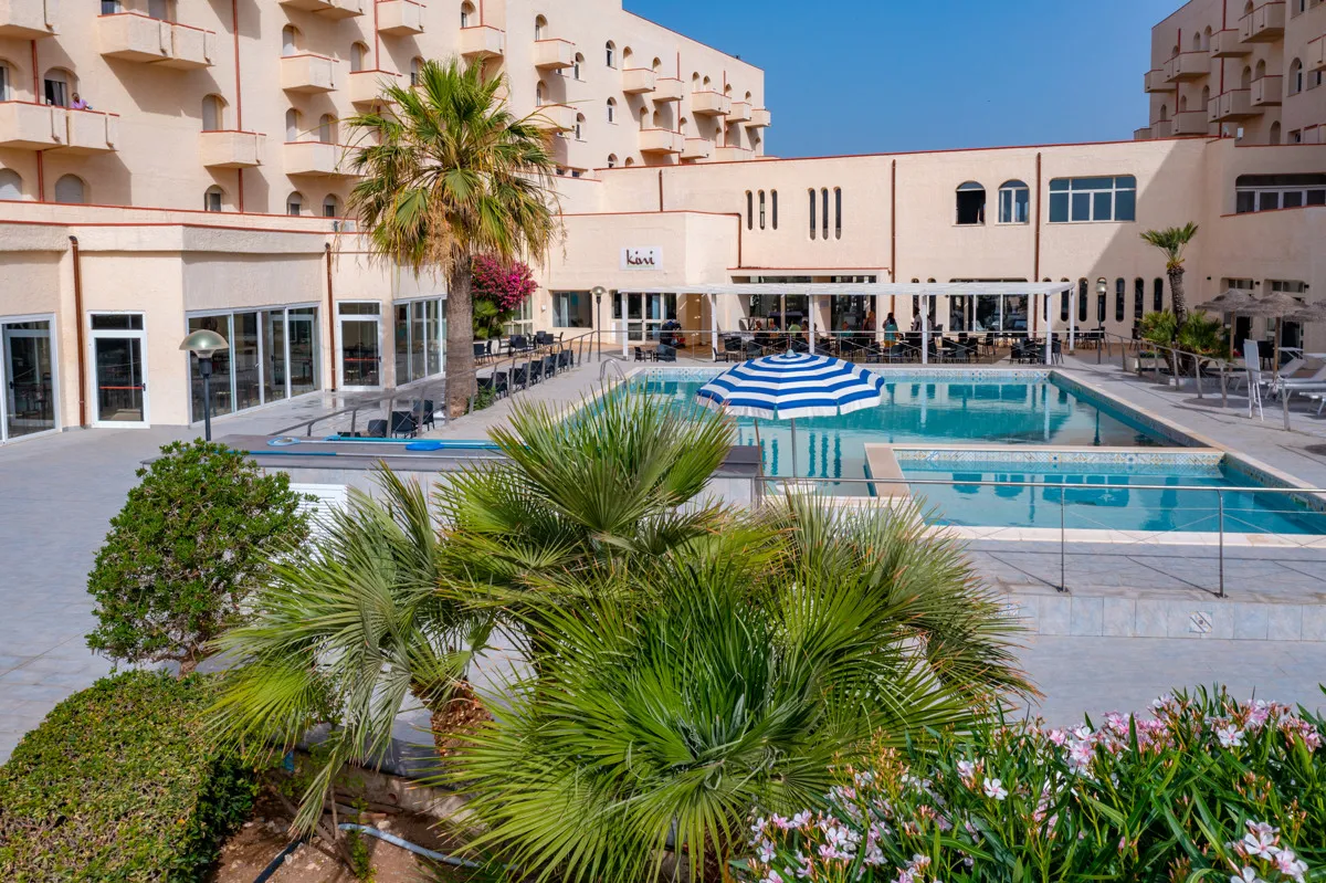 Area piscina con ombrellone a righe blu e vegetazione tropicale