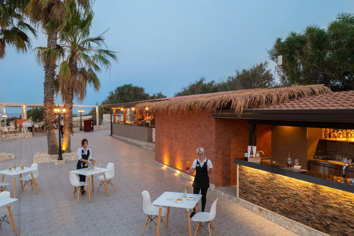 Bar esterno al tramonto con cameriere e tavolini illuminati
