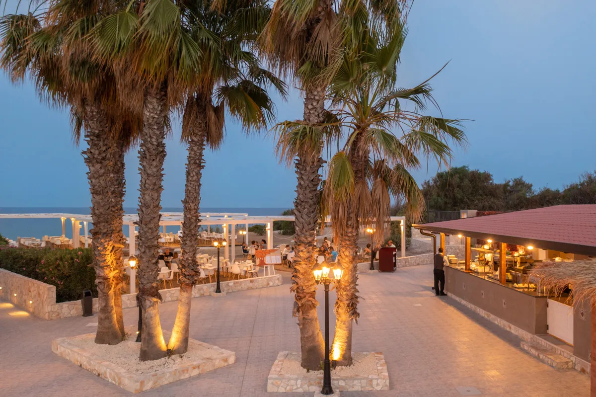 Ristorante all'aperto serale con palme illuminate e vista mare