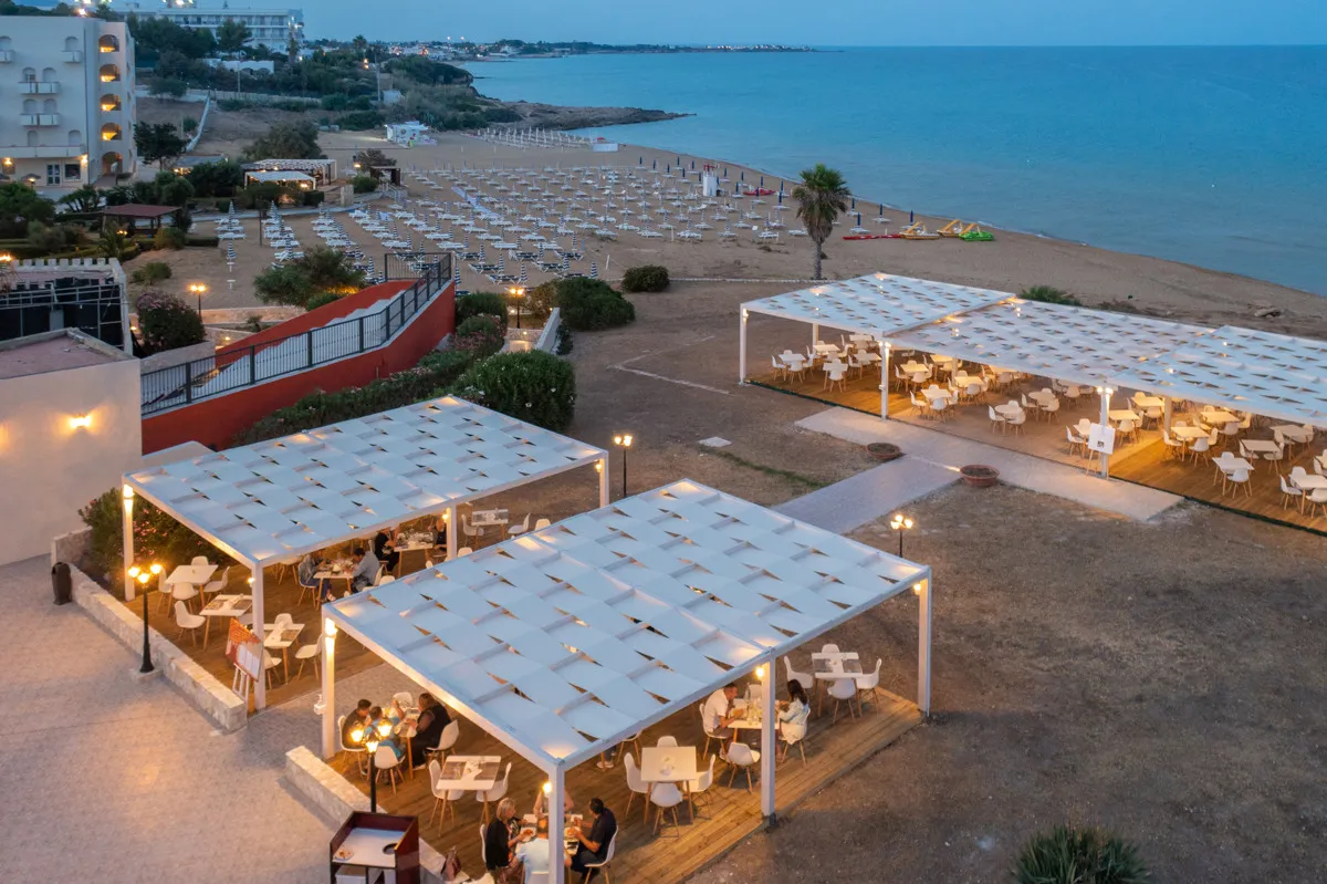 Ristorante all'aperto al crepuscolo con pergole bianche e vista mare