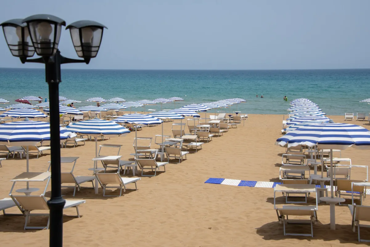 Spiaggia con ombrelloni a righe blu, lettini e mare azzurro
