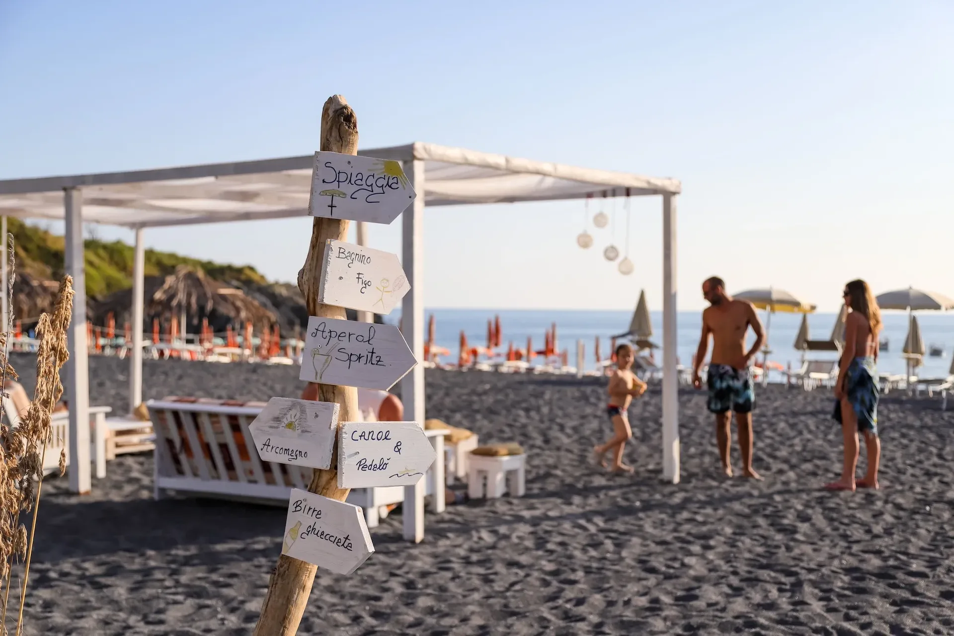Spiaggia attrezzata con cartelli, gazebo bianco e bagnanti sul mare