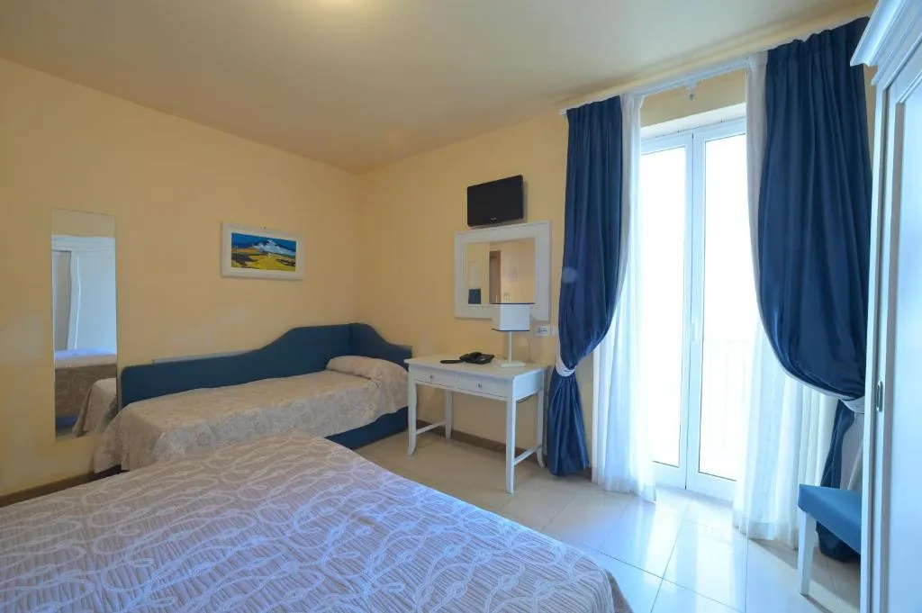 Camera con pareti gialle, divano letto blu e ampia portafinestra con tende blu