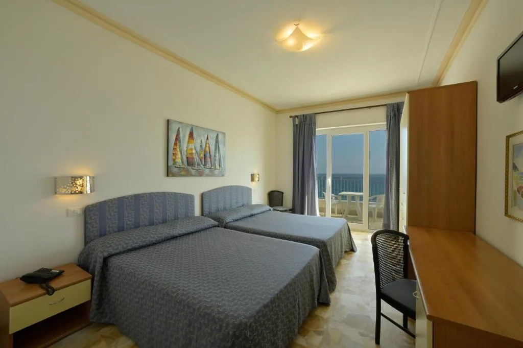 Camera doppia con letti separati, testiere blu e balcone affacciato sul mare