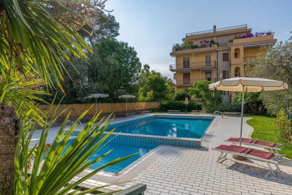 Piscina circondata da pavimentazione, lettini rossi, ombrelloni e giardino con palme