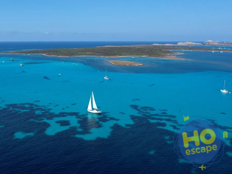 Mare turchese con barca a vela e isolotto verde all'orizzonte