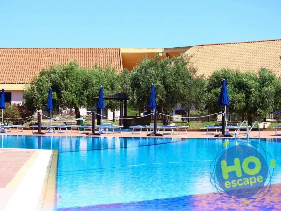 Piscina con lettini, ombrelloni blu e ulivi accanto agli edifici del resort