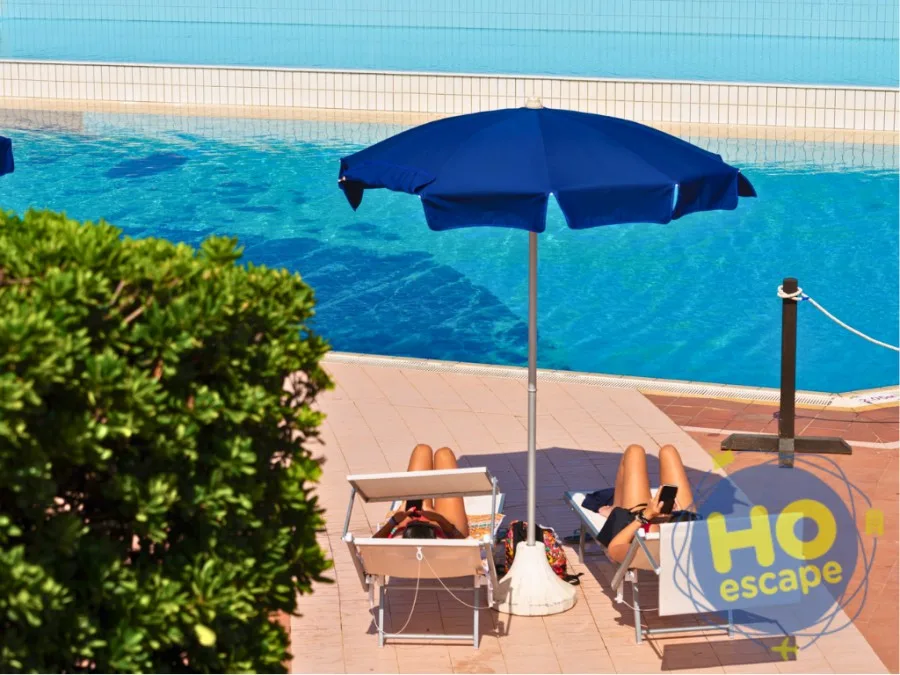 Ospiti in relax su lettini con ombrellone blu a bordo piscina