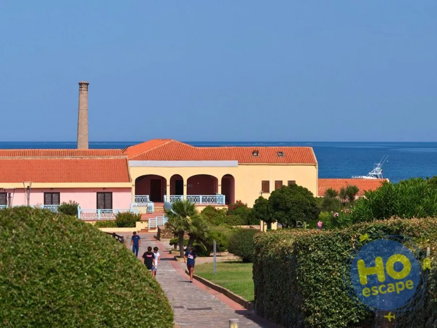 Edifici del resort con vista sul mare, ciminiera storica e vialetto pedonale alberato