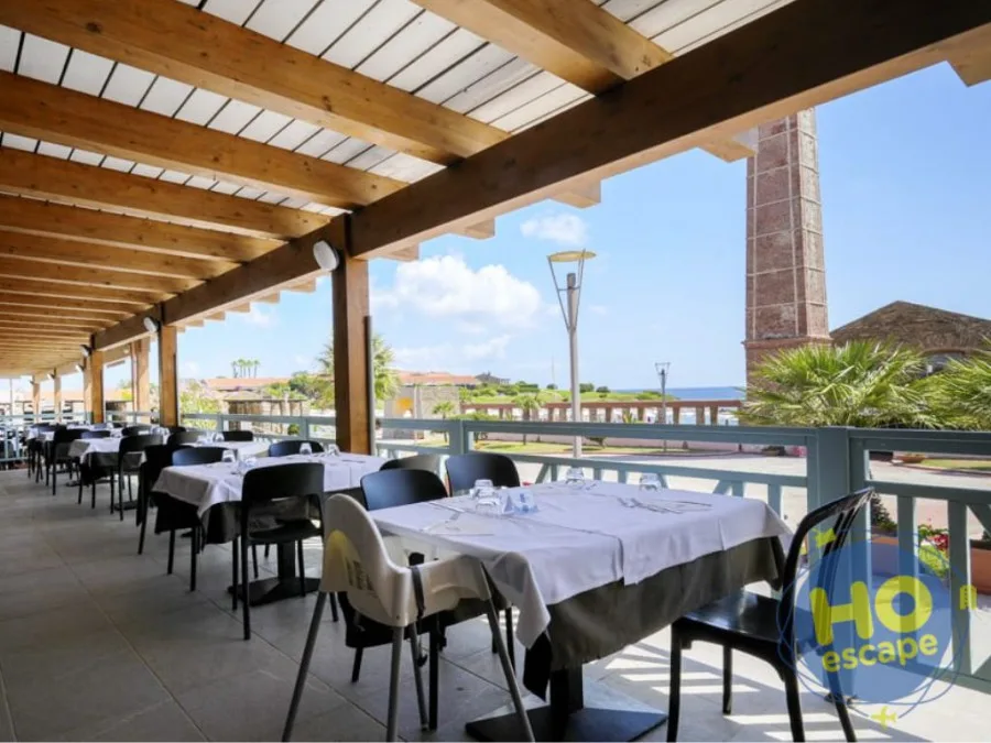Terrazza del ristorante con pergolato in legno, tavoli apparecchiati e vista sul mare e ciminiera