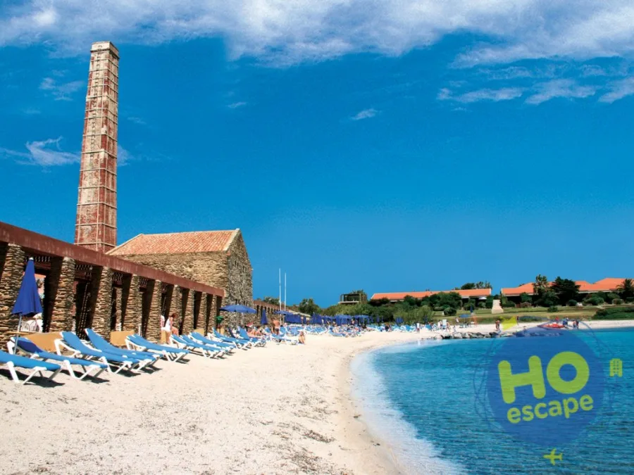 Spiaggia di sabbia bianca con lettini, ombrelloni blu, antica ciminiera e mare cristallino