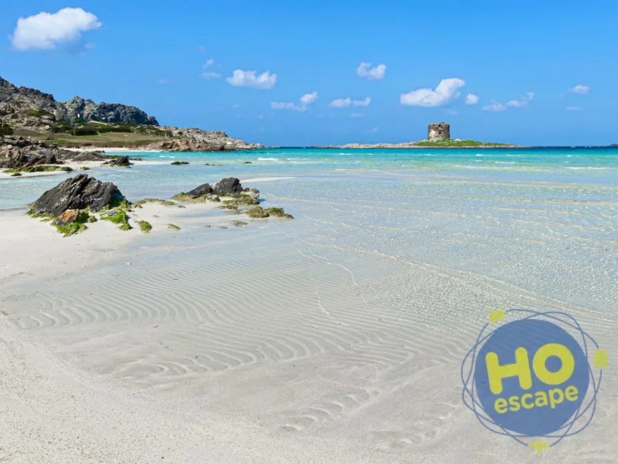 Spiaggia di sabbia bianca con acqua turchese, scogli e torre costiera all'orizzonte
