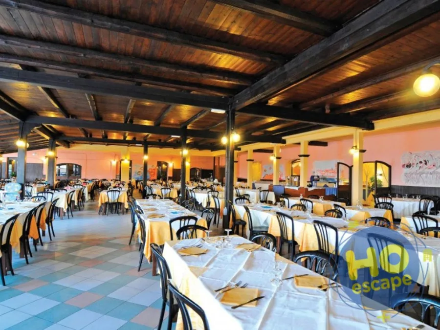 Ampia sala ristorante interna con soffitto in legno a travi e tavoli apparecchiati con tovaglie gialle e bianche