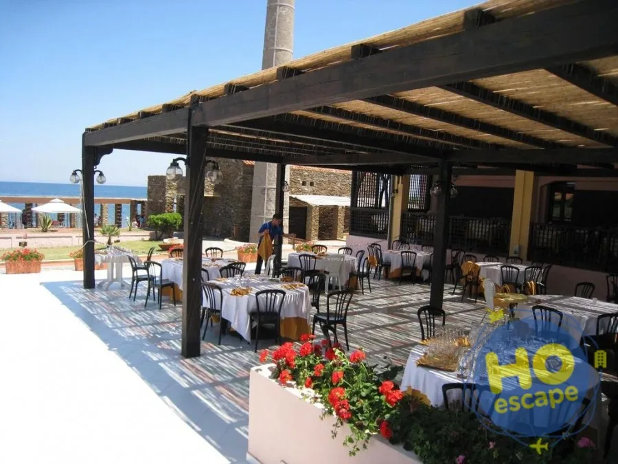 Ristorante all'aperto con pergolato in canne, tavoli apparecchiati e vista sul mare