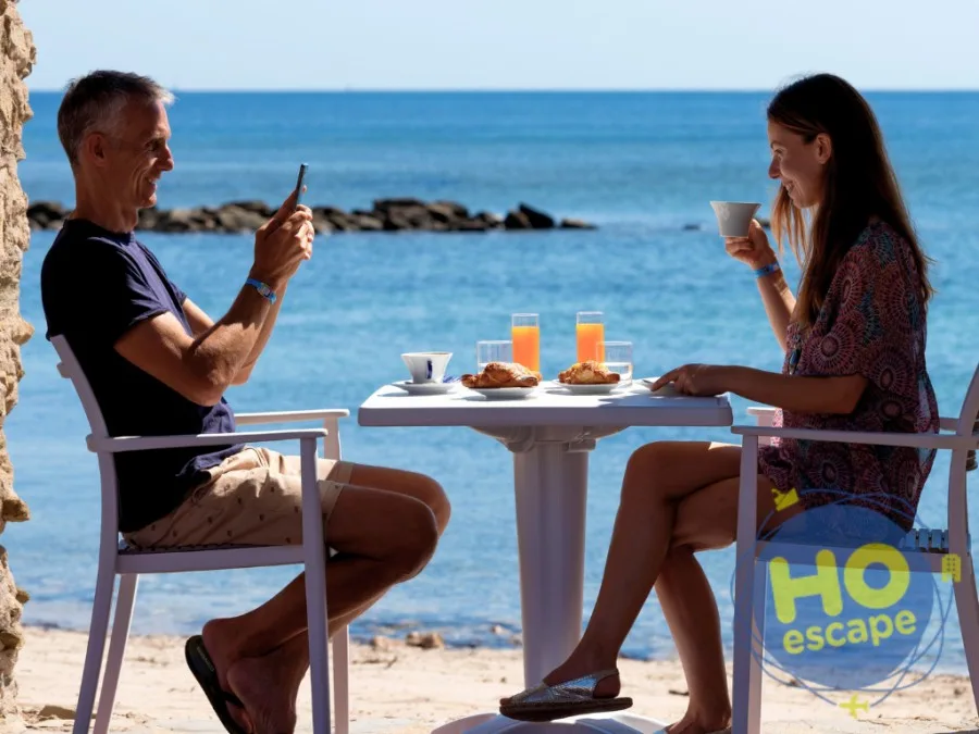 Coppia che fa colazione con cornetti e succhi a un tavolo sulla spiaggia fronte mare