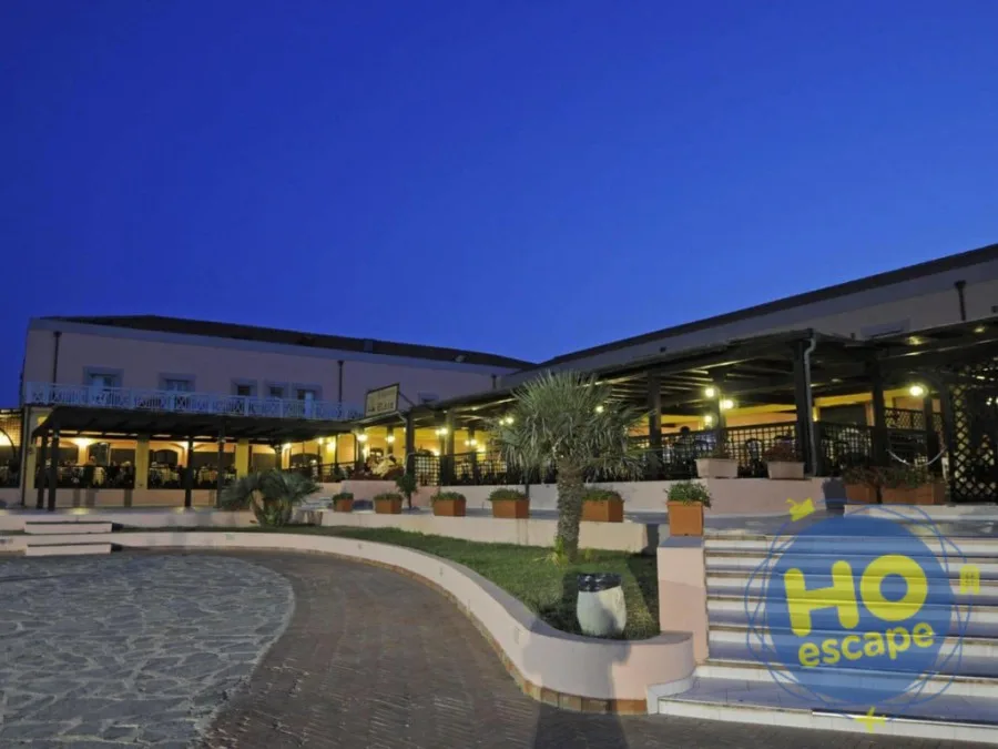 Esterno dell'hotel illuminato di sera con terrazza coperta e giardino con palme