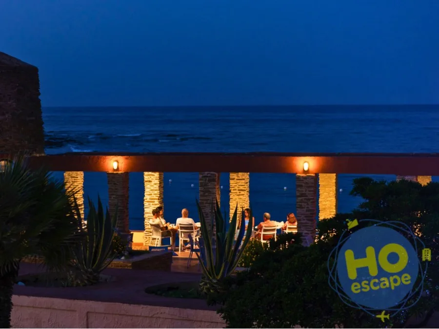 Terrazza serale con ospiti ai tavoli e vista sul mare al tramonto