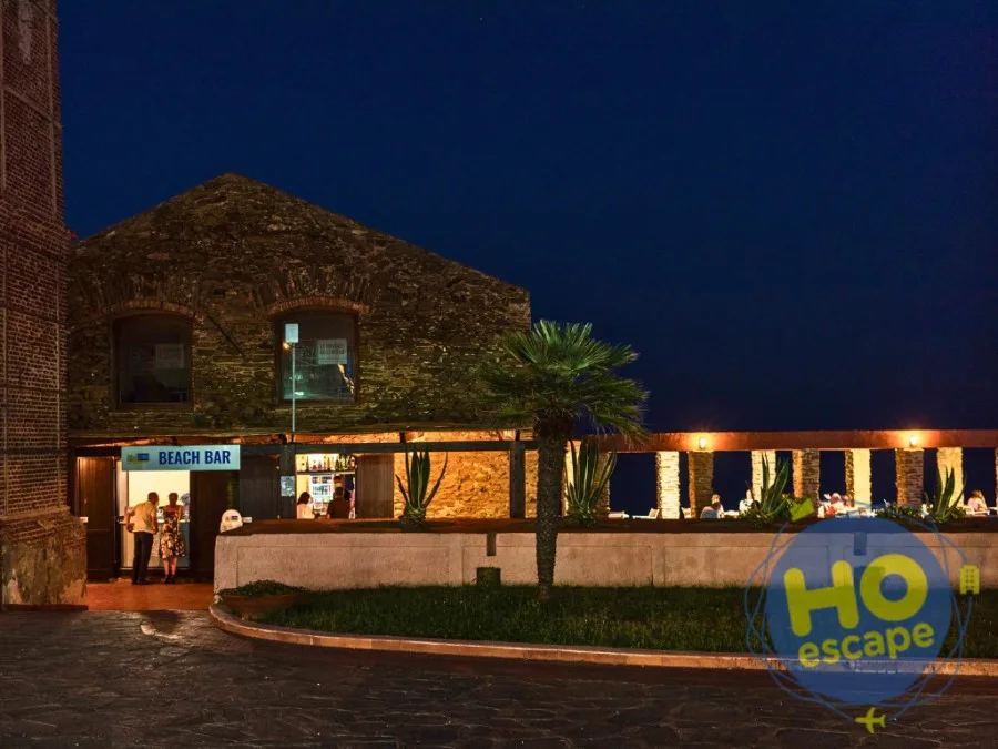Beach bar in pietra illuminato di sera con palma e terrazza affacciata sul mare