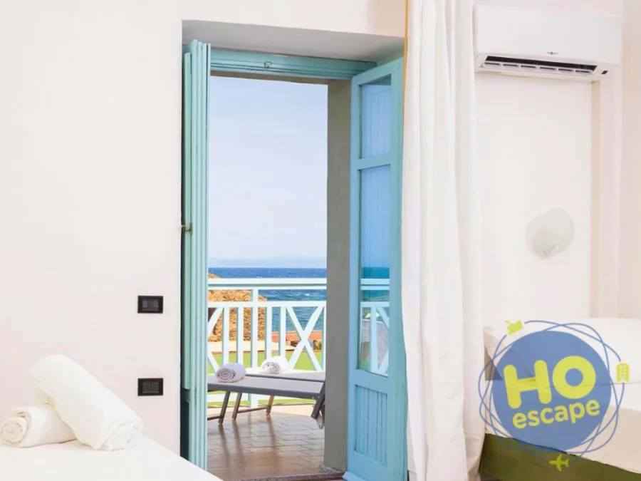 Porta-finestra con persiane azzurre aperta su balcone con vista mare