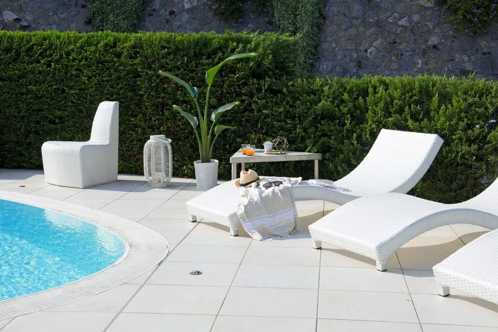 Bordo piscina con lettini bianchi, siepe verde e atmosfera rilassante
