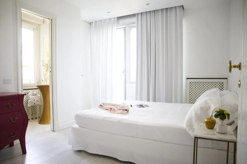 Camera luminosa con letto bianco, comò rosso e tende chiare