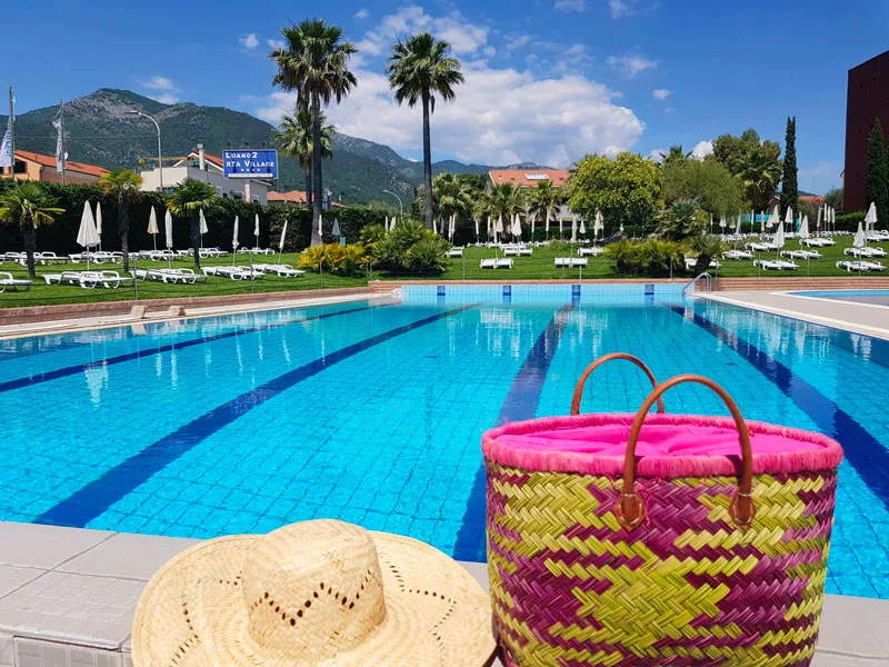 Cappello di paglia e borsa colorata a bordo piscina con palme e montagne
