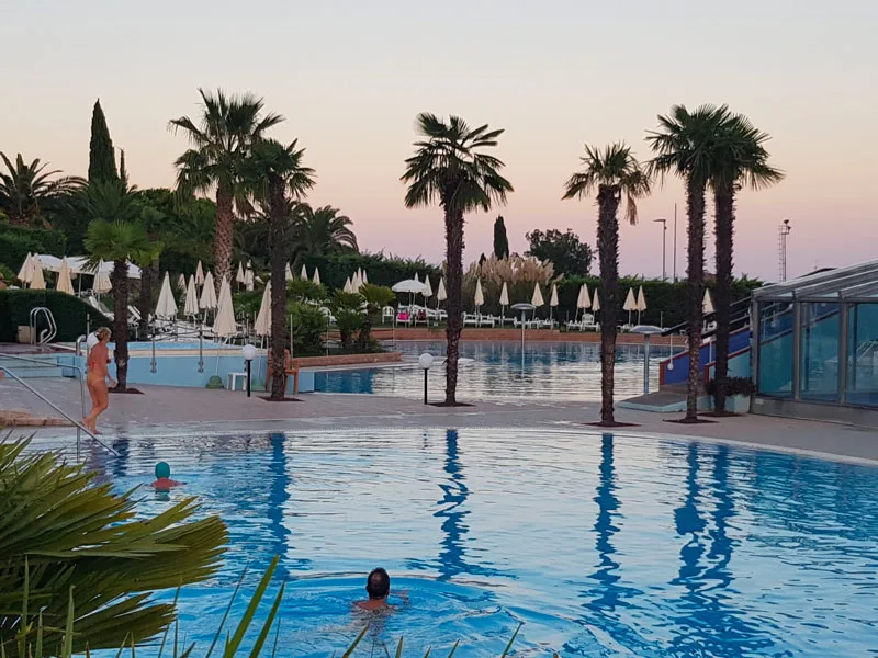 Piscina al tramonto con palme e bagnanti in un'atmosfera serale