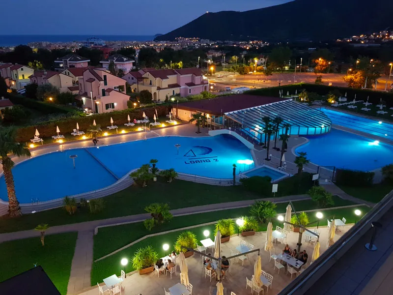 Vista notturna del resort con piscine illuminate e luci della città