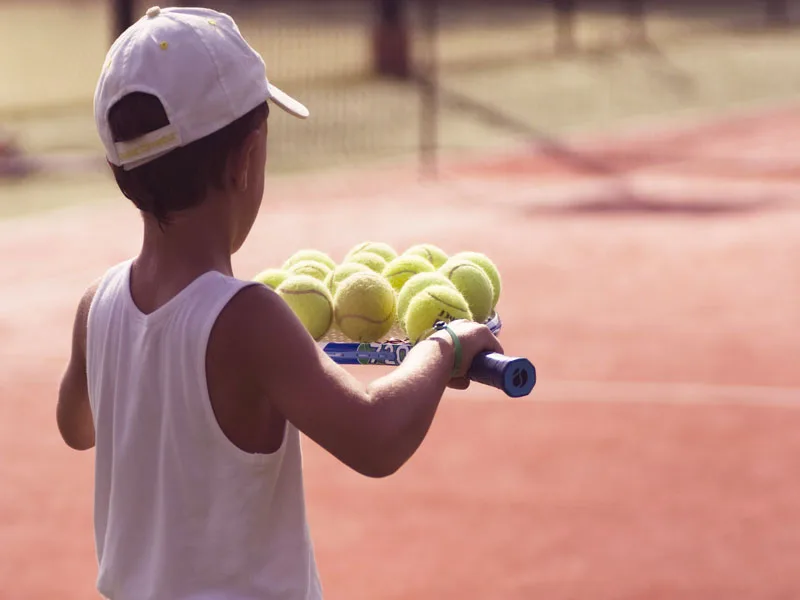 Bambino con racchetta e palline da tennis sul campo in terra rossa