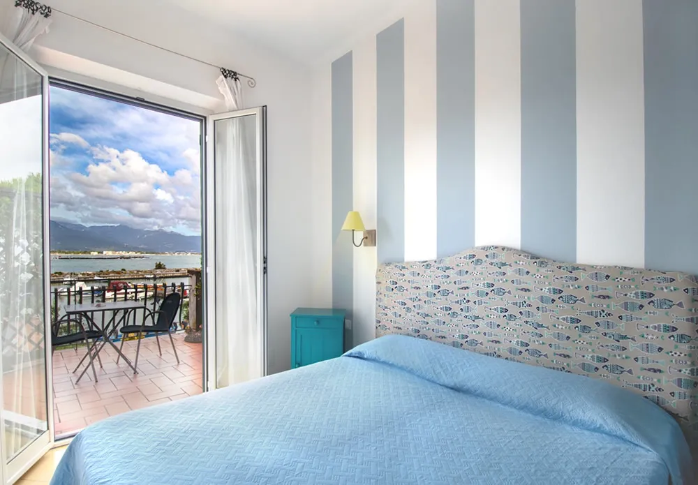 Camera con pareti a righe azzurre, letto matrimoniale e balcone con vista sul porto