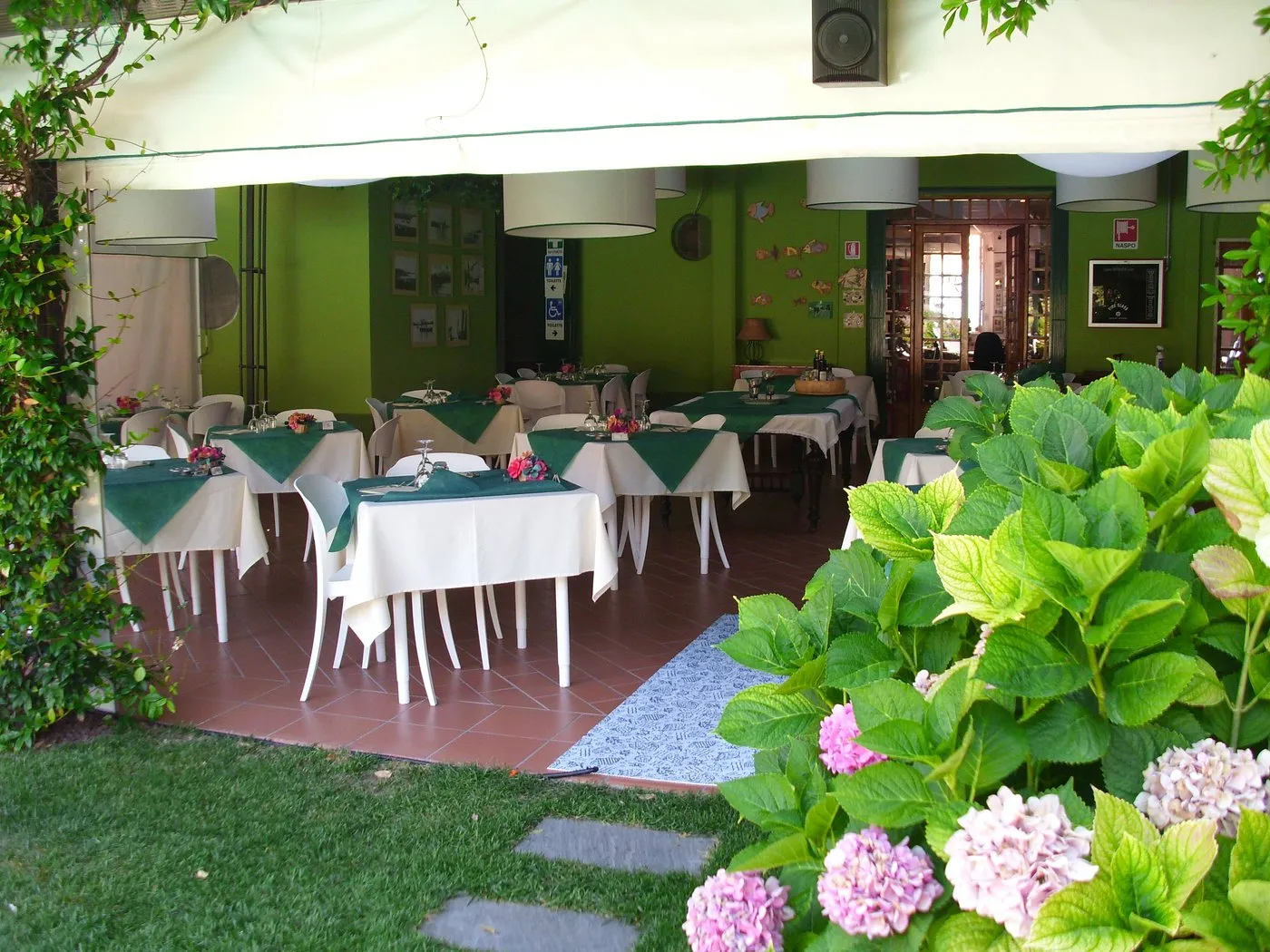 Sala ristorante verde con tavoli apparecchiati affacciata sul giardino fiorito