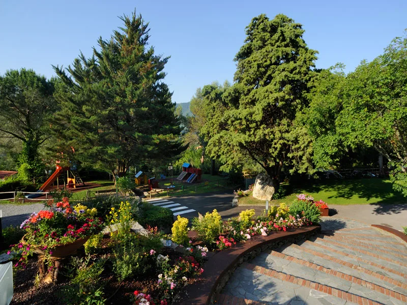 Giardino con aiuole fiorite, alberi e area giochi per bambini