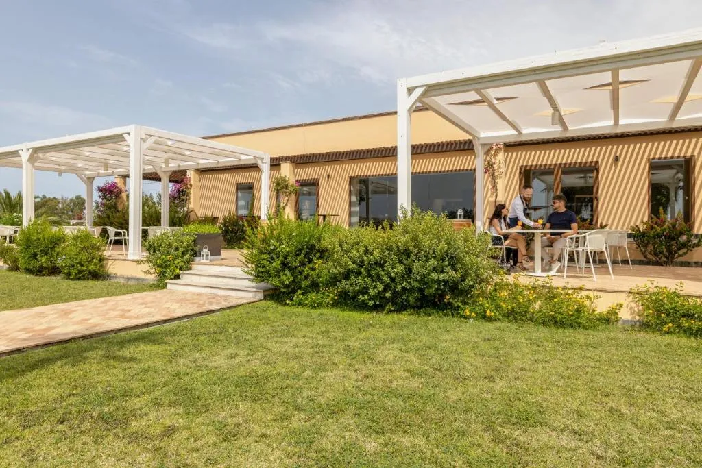 Area esterna del resort con pergole bianche, giardino e ospiti seduti a un tavolo