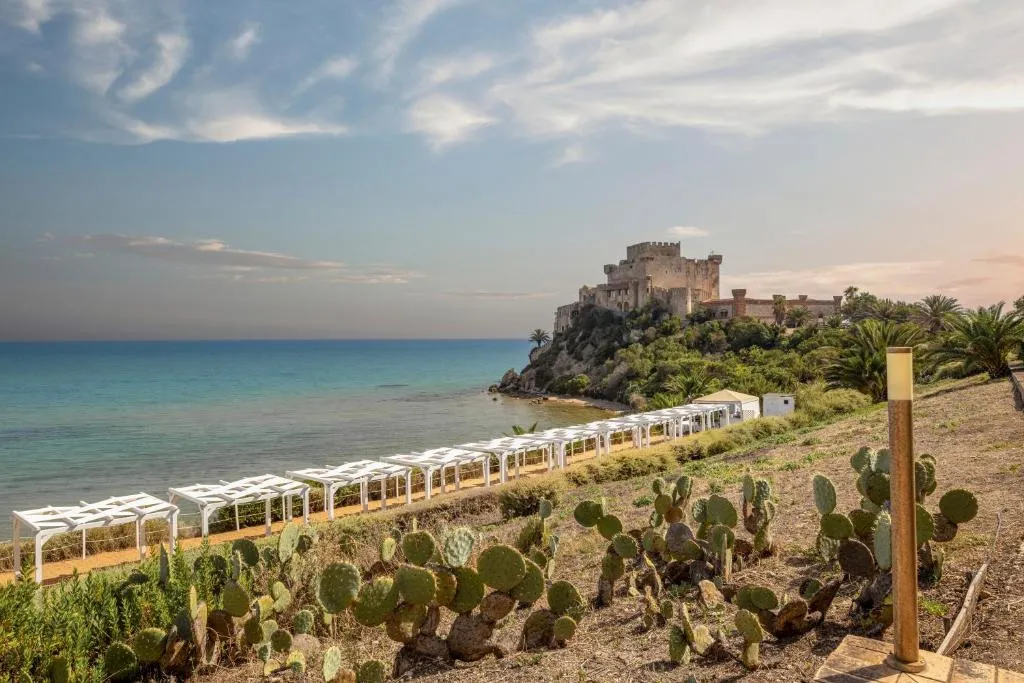 Panorama al tramonto del castello sul mare con spiaggia attrezzata e fichi d'India