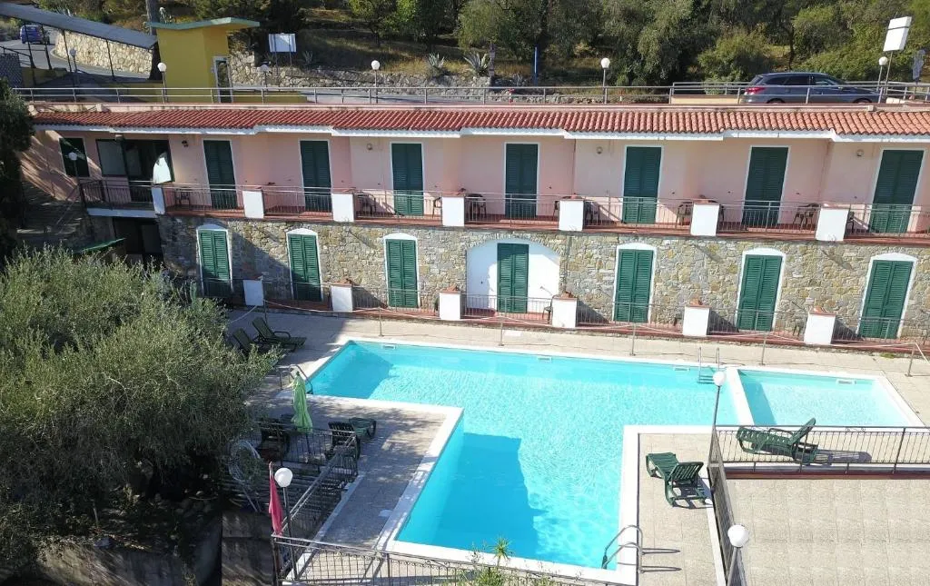 Piscina esterna con lettini e edificio con persiane verdi sullo sfondo