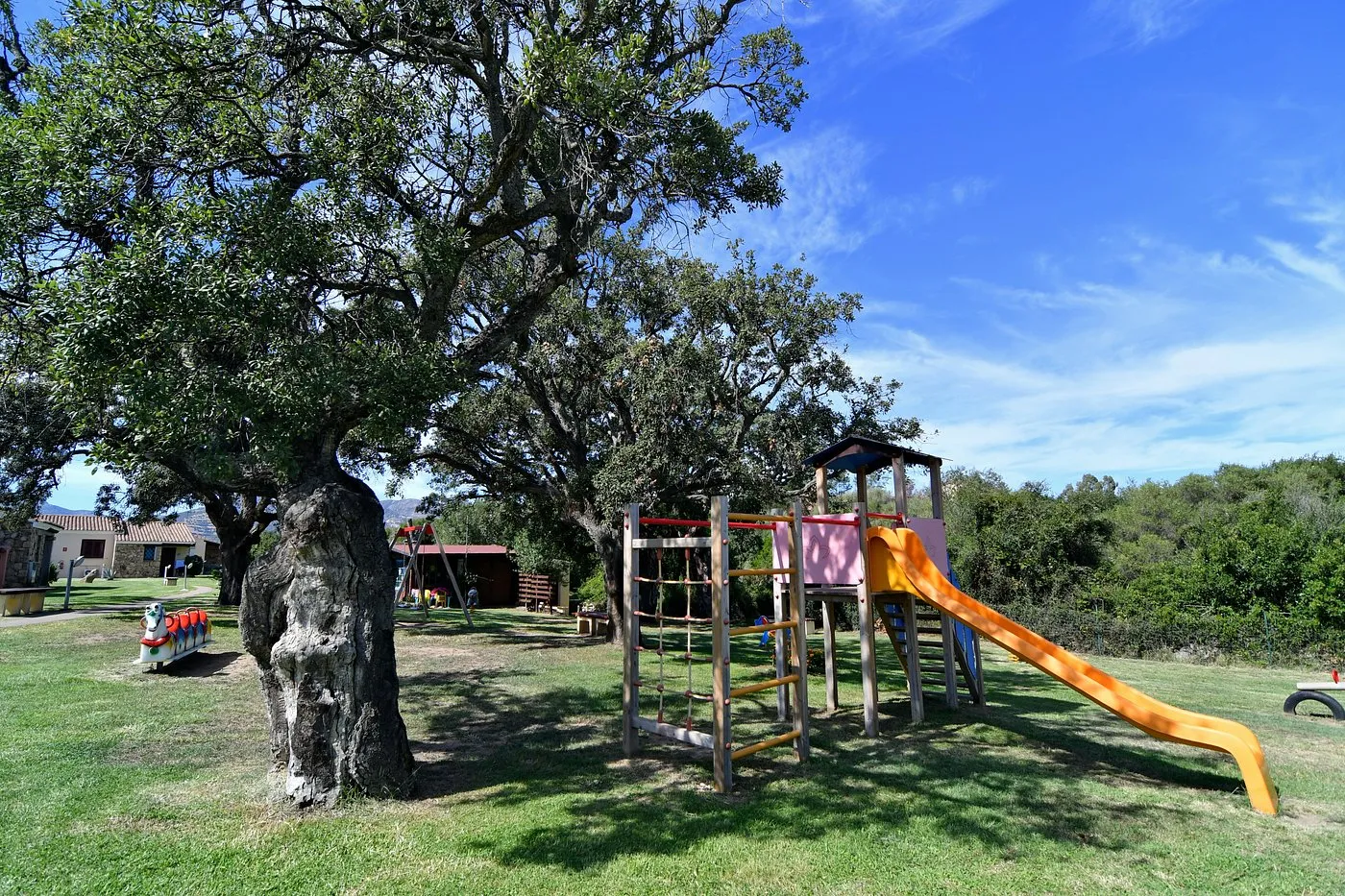 Parco giochi per bambini con scivolo e arrampicata sotto grandi alberi