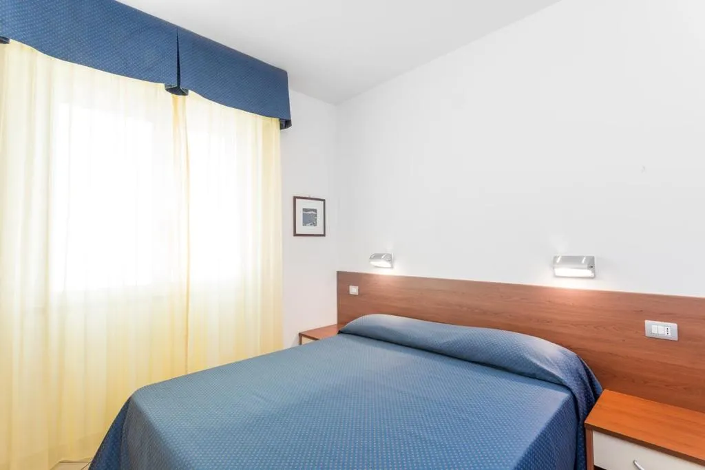 Camera matrimoniale con letto azzurro, testiera in legno e tende chiare