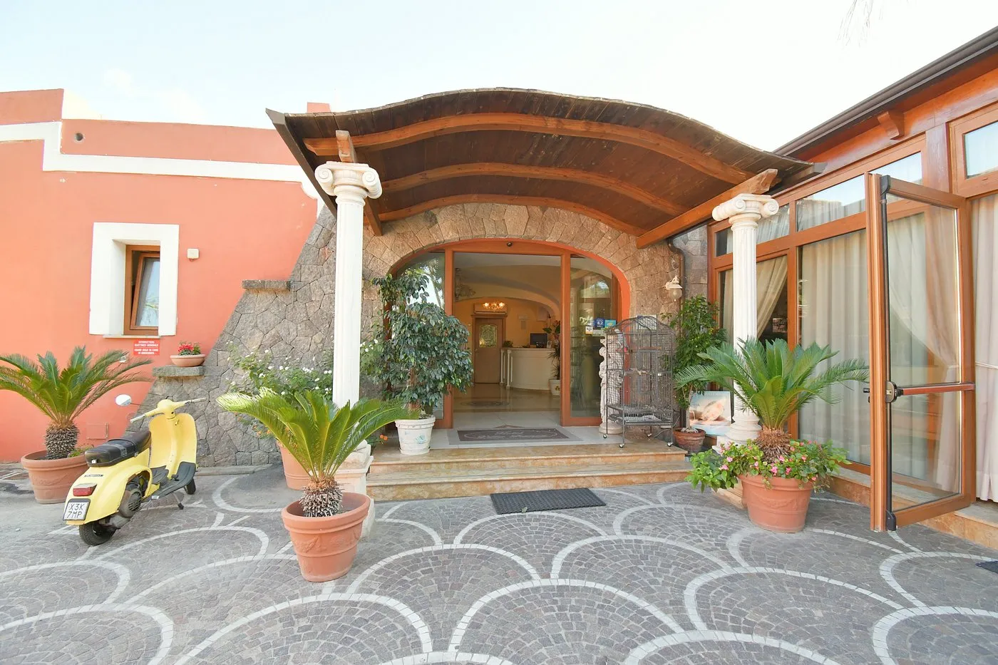 Ingresso dell'hotel con colonne, pergola in legno e piante in vaso