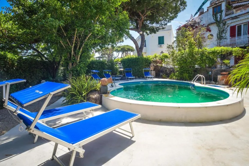 Piscina rotonda con lettini blu tra il verde e gli edifici dell'hotel