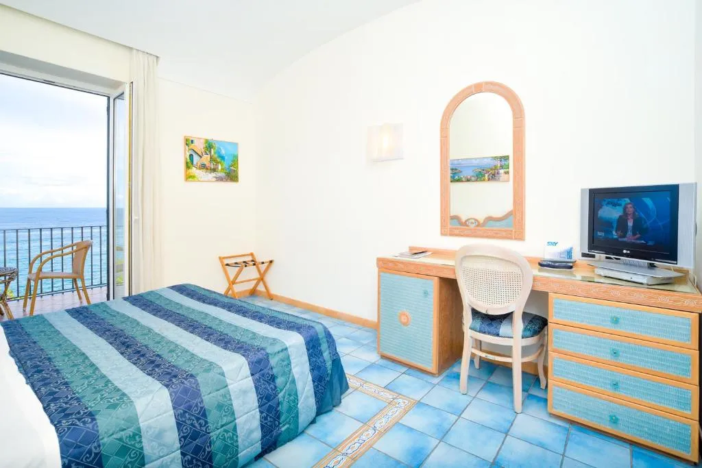 Camera con scrivania, TV e balcone affacciato direttamente sul mare