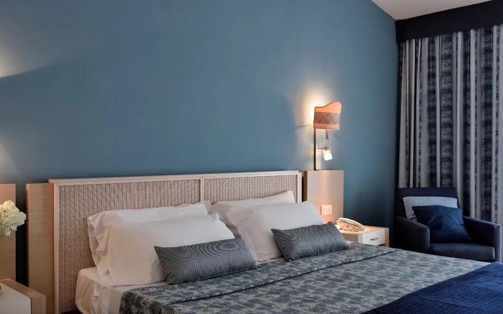 Camera matrimoniale con parete azzurra, letto con cuscini grigi e poltrona