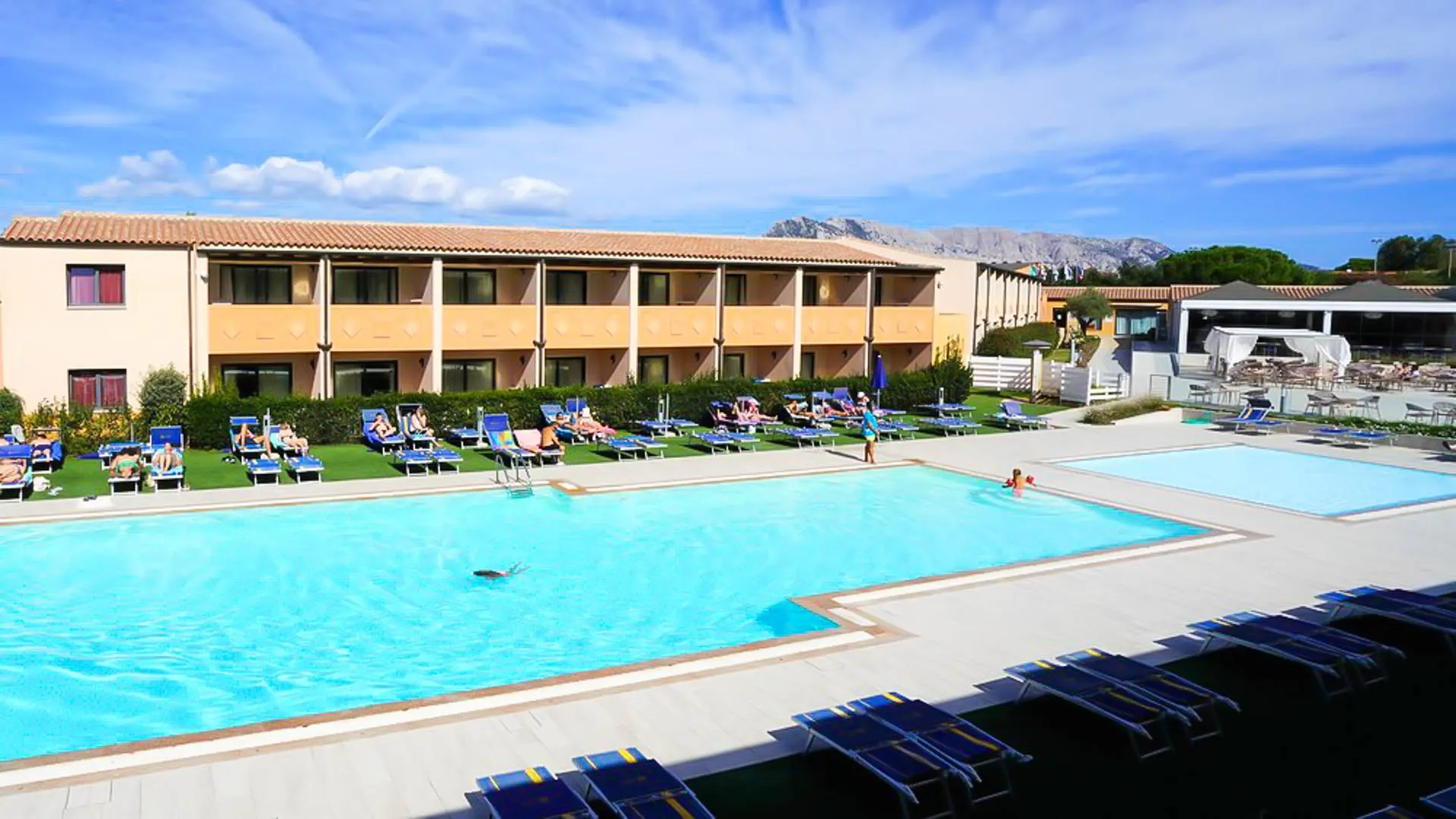Ampia piscina esterna con lettini blu sul prato e vista sulle montagne