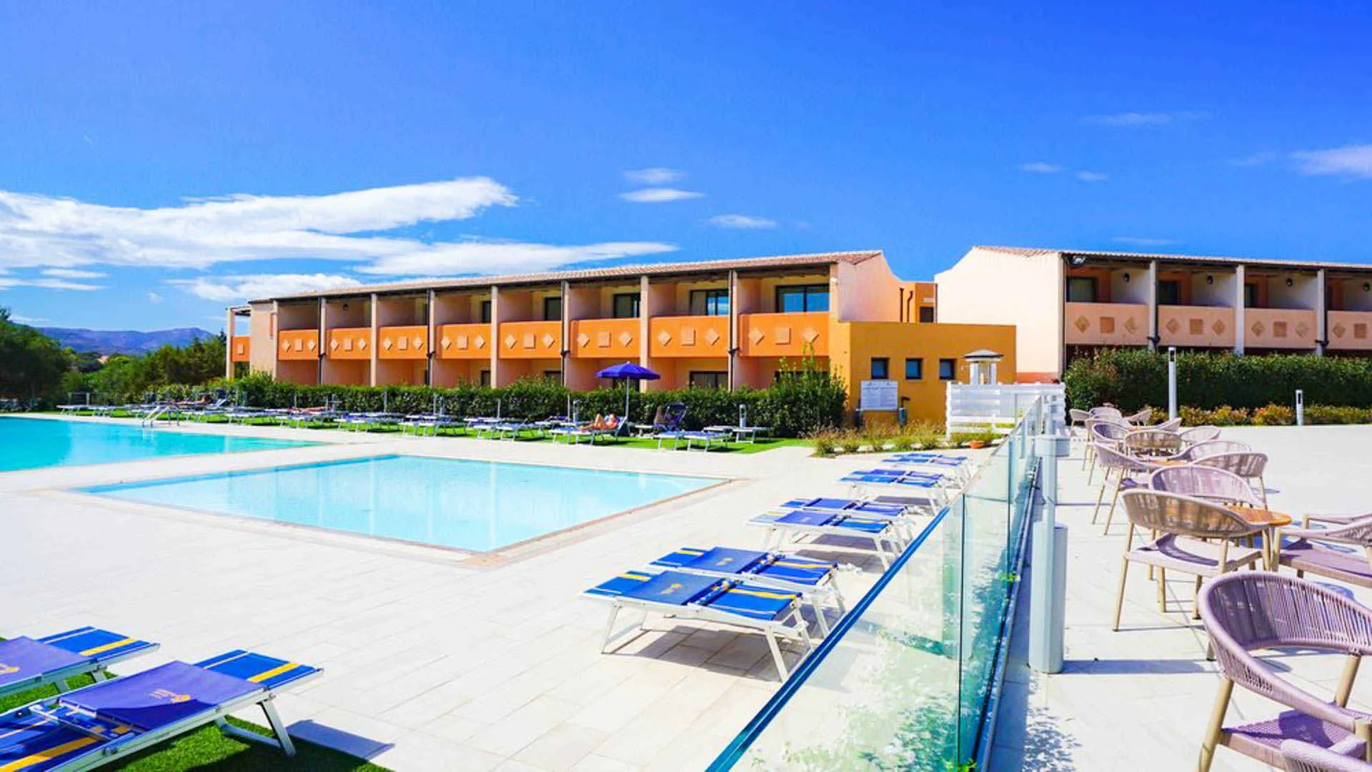 Piscine esterne con lettini blu e area relax con poltroncine davanti agli edifici del resort