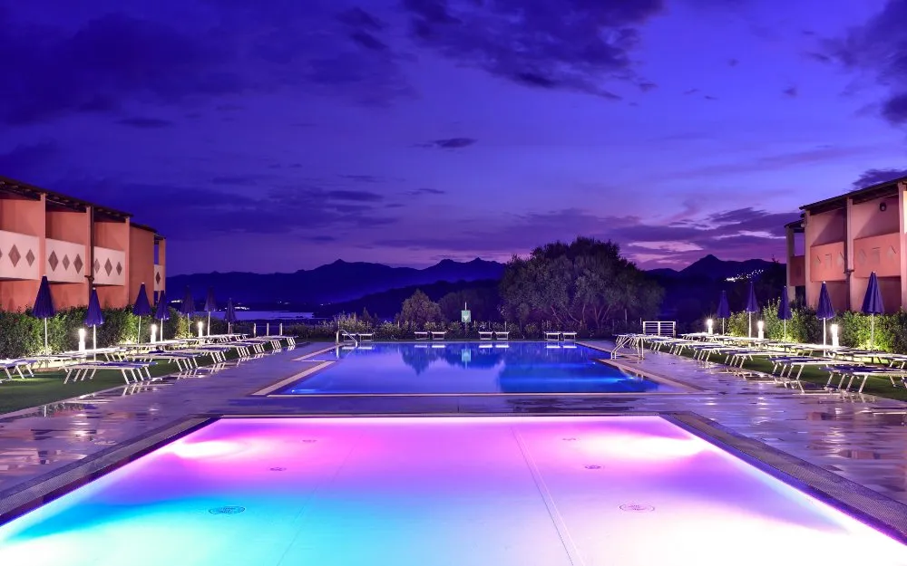 Piscine illuminate al tramonto con luci rosa e azzurre e vista sulle montagne
