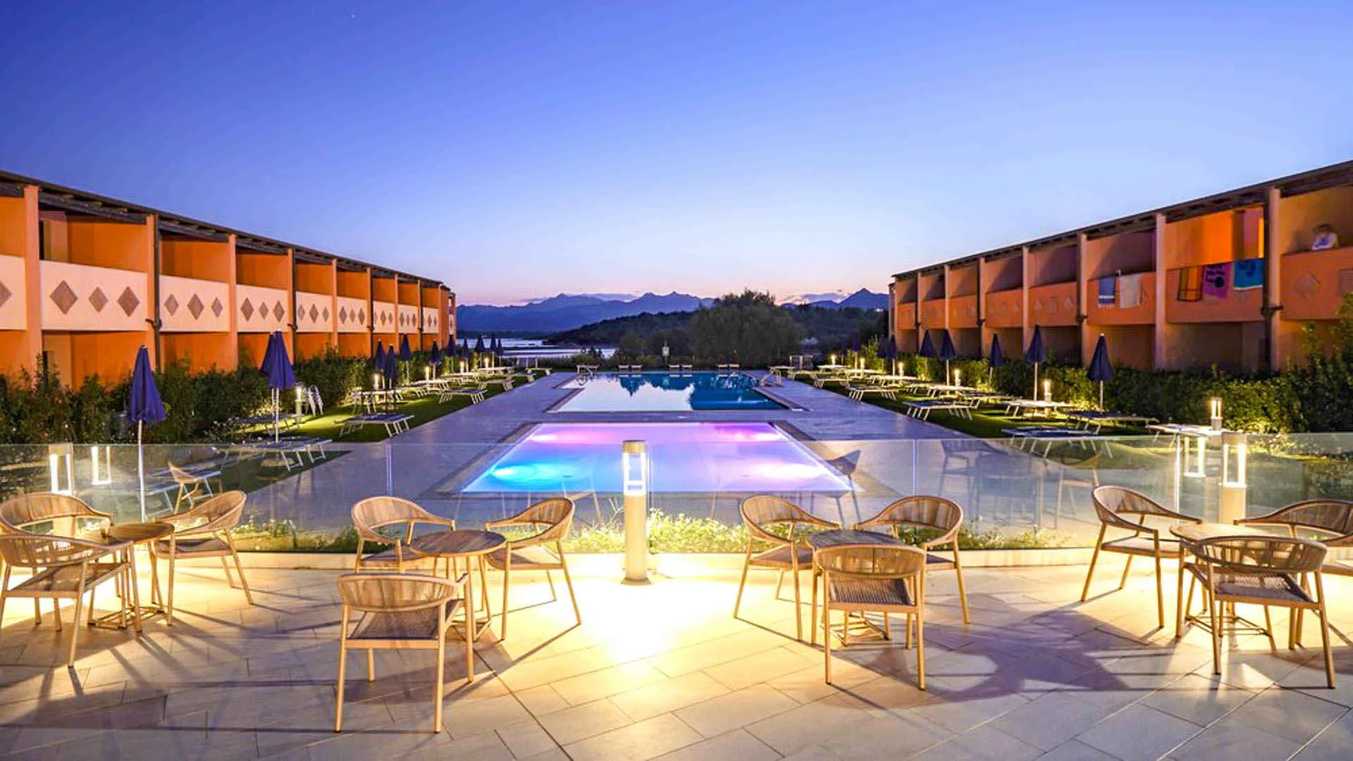 Piscina del resort illuminata al tramonto con area relax e tavolini in primo piano