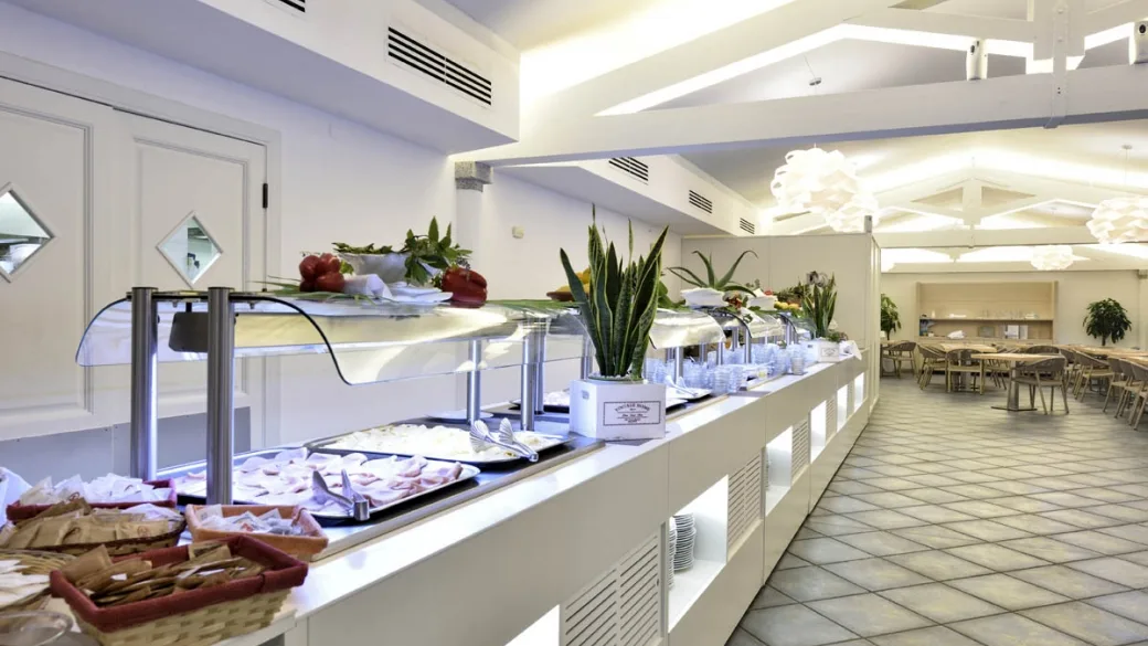 Buffet del ristorante con banco refrigerato, piante decorative e sala da pranzo sullo sfondo