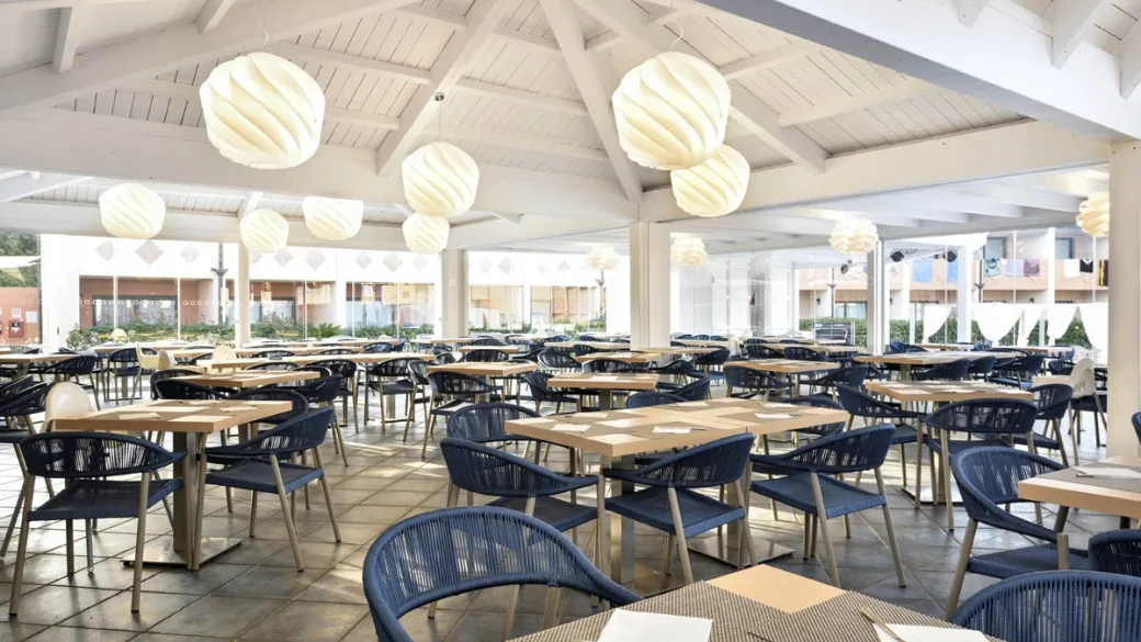 Ampia sala ristorante con tavoli in legno, sedie blu e lampadari decorativi
