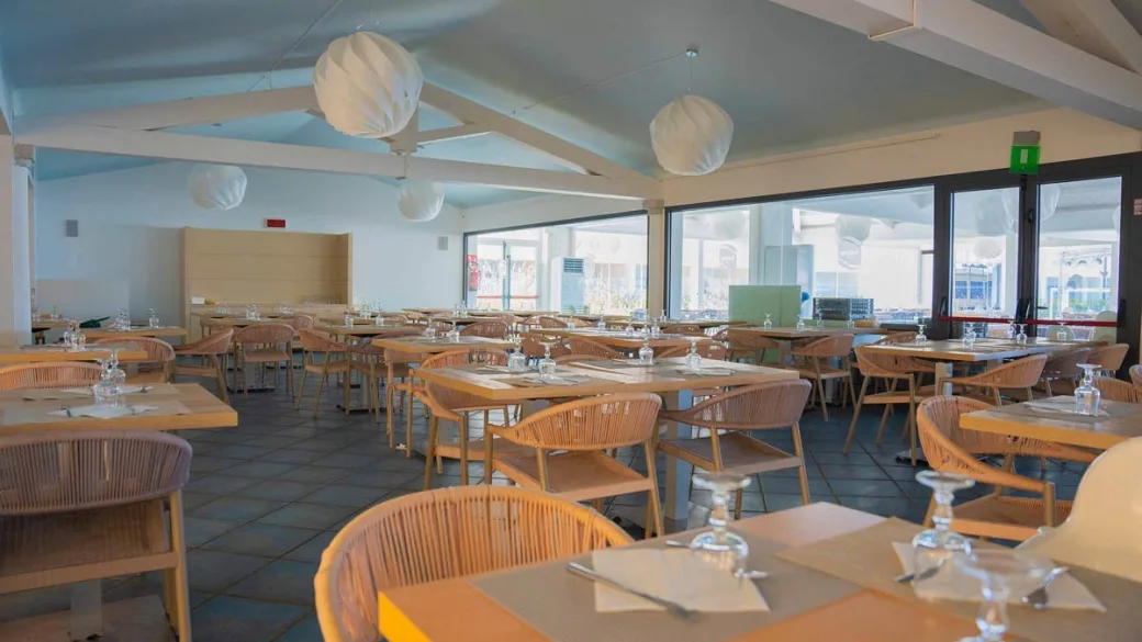 Sala ristorante luminosa con tavoli in legno e sedie in corda chiara
