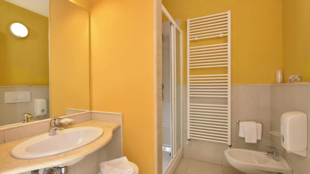 Bagno della camera con pareti gialle, lavabo, specchio, doccia e scaldasalviette